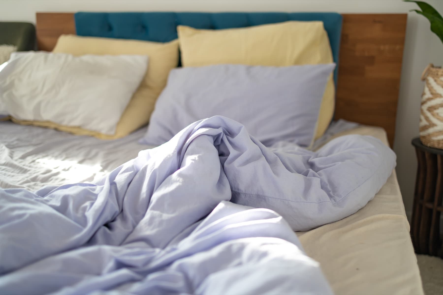Bed with a rumpled lavender duvet and pastel pillows